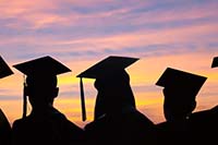 Photo of graduates wearing caps against a sunset